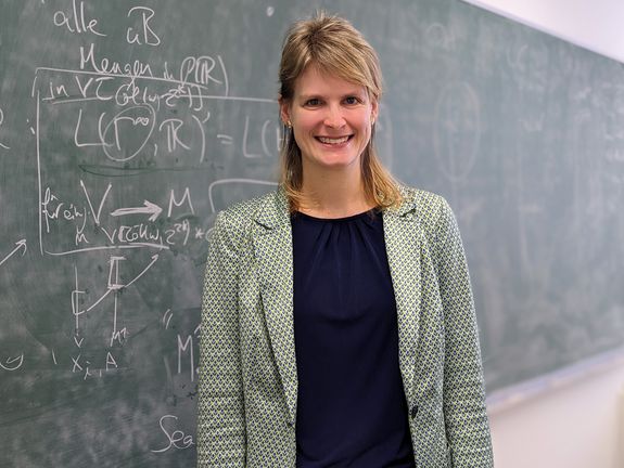 Porträt Sandra Müller vor grüner Tafel mit mathematischen Formeln in weiß