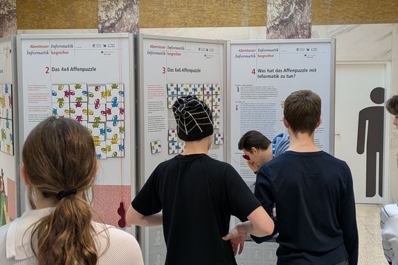 Plakatwände, davor Menschen mit Rücken zur Kamera