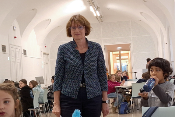 Vizerektorin Koch steht bei einer sitzendenden Kindergruppe und blickt in die Kamera