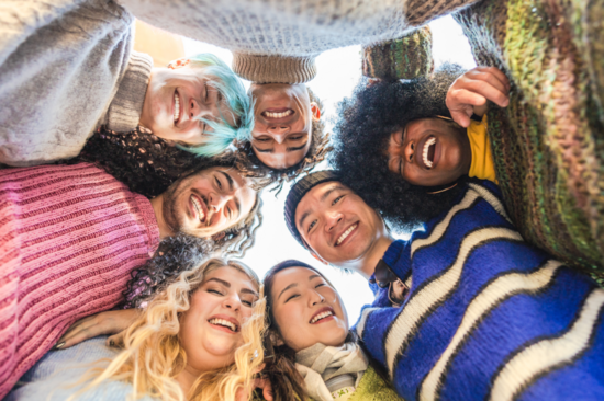 Seven young people stand in a circle and look down into the camera