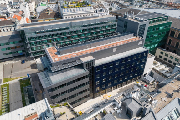 Drohnenbild des Campus Getreidemarkt mit dem langgestreckten Bauteil BF. Oben ist ein L-förmiger oranger Streifen sichtbar.