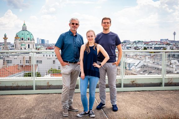 Drei Personen auf einer Dachterrasse, dahinter die Wiener Karlskirche
