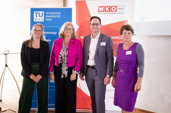 Gruppenbild mit vier Personen vor einem TU-Aufsteller und einem WKO-Aufsteller. Heller Raum.