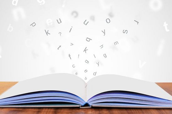 A book lies open on a wooden surface. The pages of the book are blank. The letters float above and around the book.