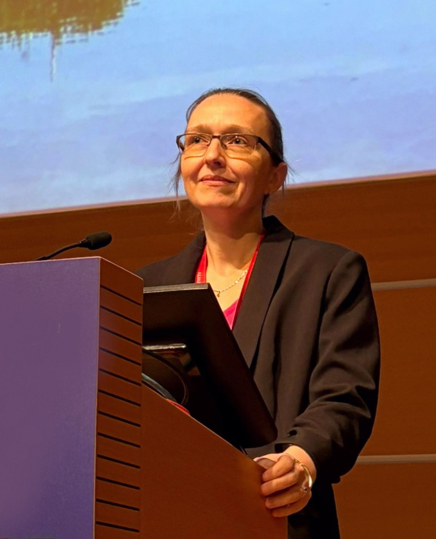 Porträt Hana Krasna, Frau mit Brille und dunklem Oberteil bei Pult mit Mikrofon