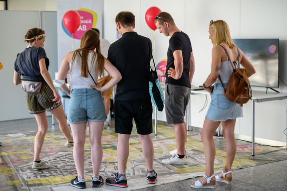 Auf dem Boden liegt ein riesiger Stadtplan-Teppich. Wissenschaftlerin und Besucher_innen stehen darauf.
