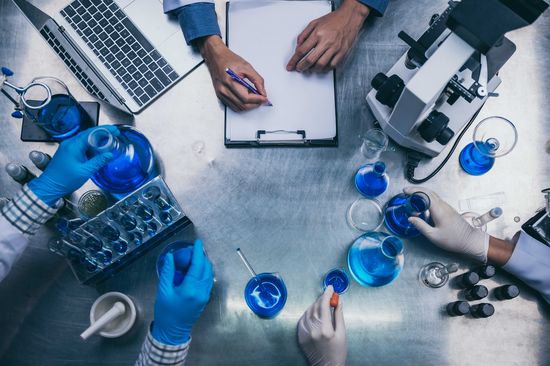 Aufsicht auf einen Tisch: Hände in Handschuhen verschieben chemische Proben in Reagenzgläsern