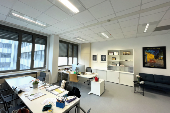 Büroraum, Fenster links, Schreibtische stehen an der Breitseite, in den Farben schwarz-weiß-grau gehalten.