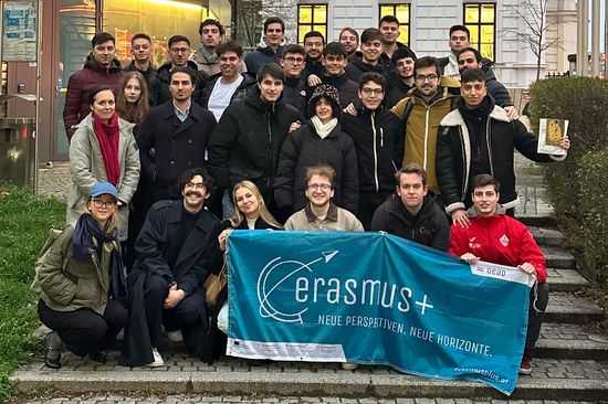 Gruppenfoto: Menschen sitzend und stehend draußen auf Stufen, Erasmus-Banner in türkis in der ersten Reihe