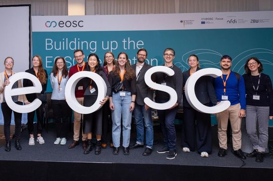 Team of Symposium Support Team standing on stage, holding up the letters EOSC