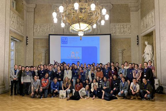 Gruppenfoto Mentoringprogramm vor Leinwand, darüber Kronleuchter