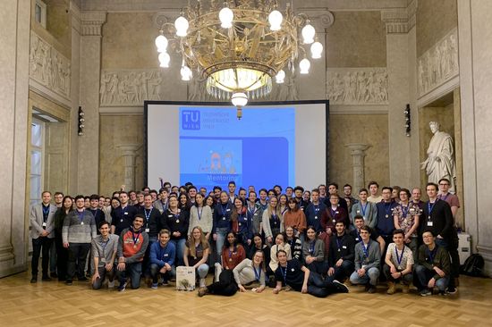 Gruppenfoto Mentoringprogramm vor Leinwand, darüber Kronleuchter