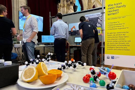 Zitronen und Molekül-Modelle auf einem Tisch, im Hintergrund Menschen die sich unterhalten. 