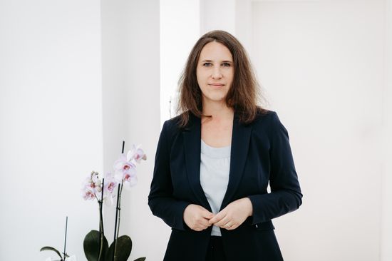 Porträt Barbara Orazume; Frau stehend mit dunklem Blazer, links daneben Orchidee