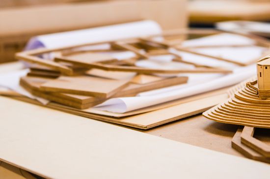 Ein Modell eines Hauses auf einem Berg, gemacht aus Karton, steht auf einem Tisch, umgeben von den übrig gebliebenen Kartonteilen