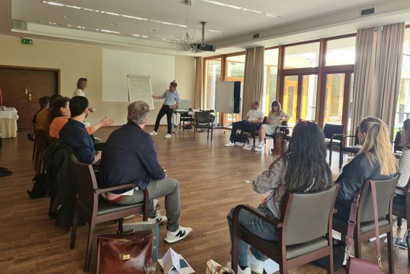 Seminarraum, Vortragender steht bei Flipchart, Studierende sitzen im Kreis auf Sesseln