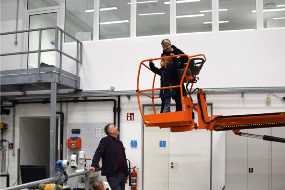 Kind mit erwachsener Person auf roter Hebebühne.