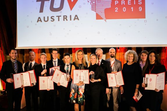 Gruppenfoto der Preisträger_innen vor einer TÜV Austria Wand auf der Bühne des Kuppelsaals.
