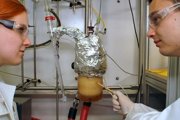 Zwei Personen gegenüber voneinander, dazwischen der Reaktor mit der Chemikalie