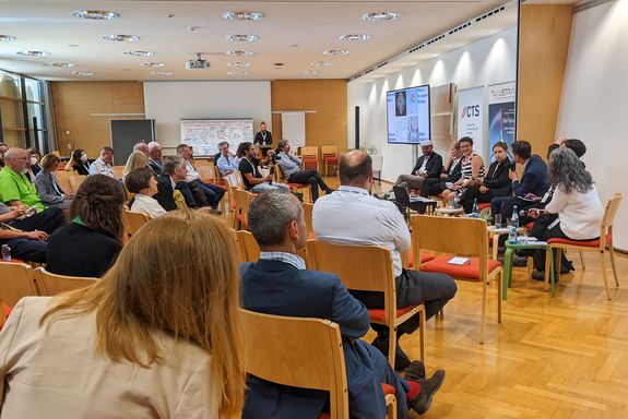 Publikum von der Seite. Am Podium die Diskussionsteilnehmenden.