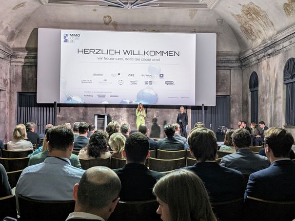 [Translate to English:] Blick Richtung Bühne mit vielen Zuhörern in den Sitzreihen