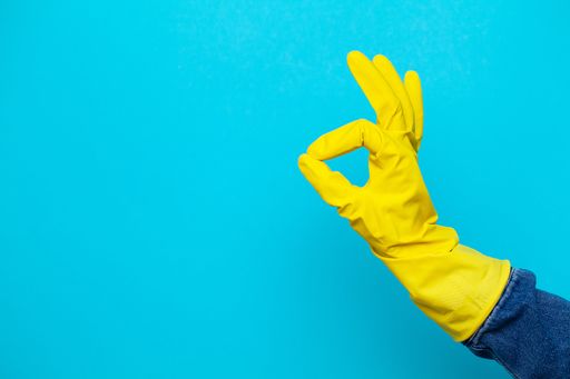 Eine Hand mit einem gelben Putzhandschuh ragt aus dem rechten Bildrand in das Bild und macht das „OK“-Zeichen.