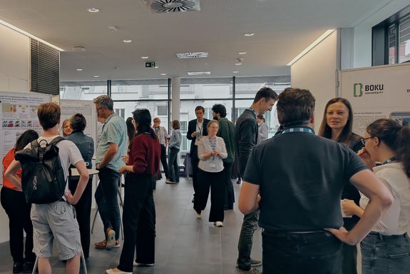 Gang mit Posterwänden und Menschen in Bewegung und im Gespräch