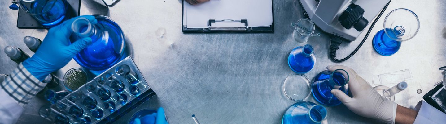 Aufsicht auf einen Tisch: Hände in Handschuhen verschieben chemische Proben in Reagenzgläsern