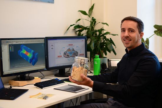 Markus Lukacevic sitzt an einem Schreibtisch und Hält ein Glas mit Sägespänen in der Hand.