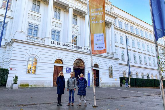 3 Personen stehen vor der Orange the World Fahne.