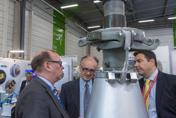 three men talking behind a helicopter gearbox