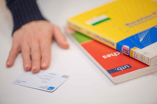 Hand auf Bibliotheksausweis, daneben zwei Bücher