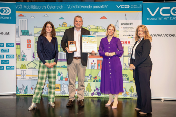 Preisverleihung des VCÖ Mobilitätspreises. Vier Damen vom VCÖ, in der Mitte Günter Emberger, der den Preis präsentiert. Im Hintergrund ein Banner mit Grafiken.