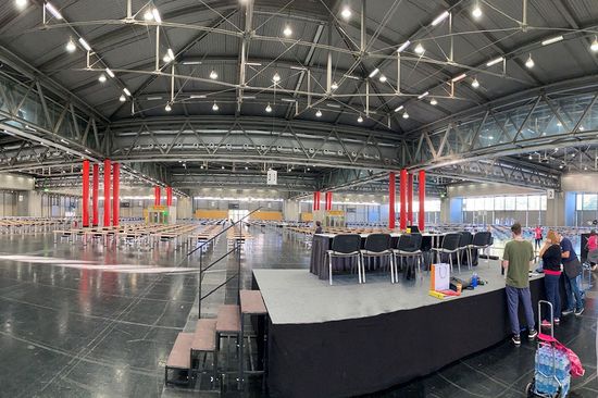 Große Halle in der Messe Wien, mittig eine Bühne, rundherum noch leere Tische.