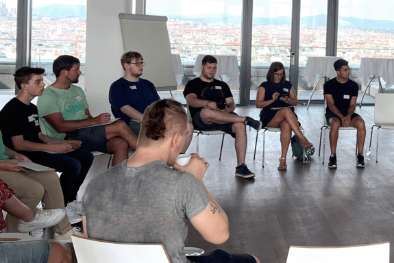 Gruppe junger Menschen im Halbkreis. Im Hintergrund Ausblick auf die Dächer Wiens.