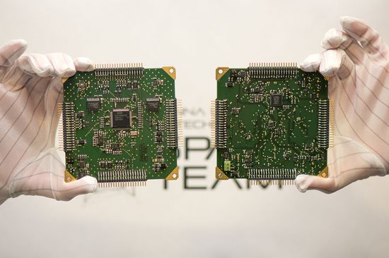 Two large computer chips are held up to the camera by hands in white gloves