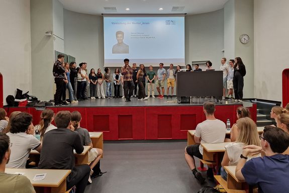 Hörsaal, Studierende sitzend von hinten, Bühne mit Studierenden stehend