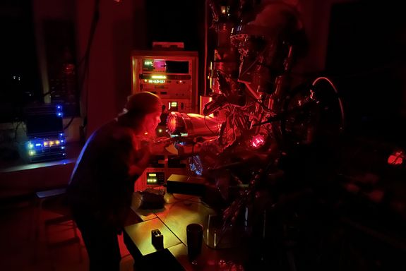 scientist in a dark room, partially illuminated by a red light source, in front of a vacuum chamber
