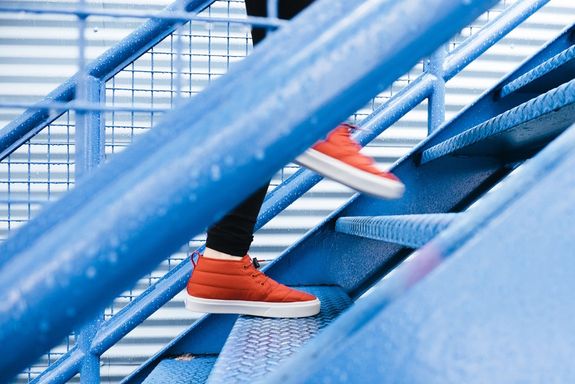 Orangene Sneakers steigen eine blau-metallische Treppe hinauf 