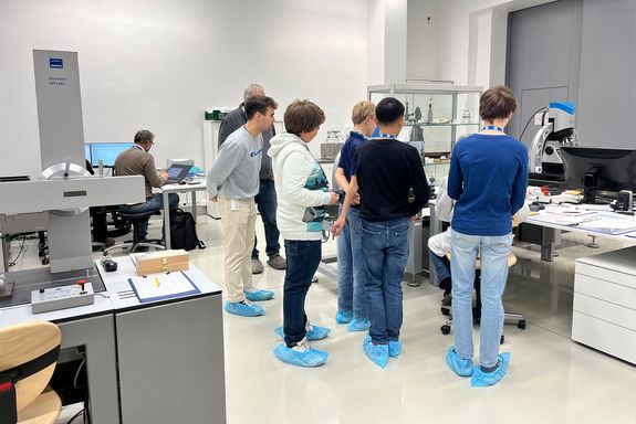 Gruppe jugendlicher steht hinter Laptop, wo Professor Station erklärt