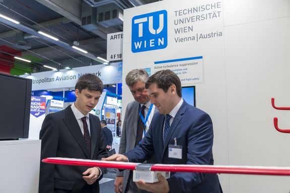 one man explains turbulence surpression to two others at the TU Wien stand