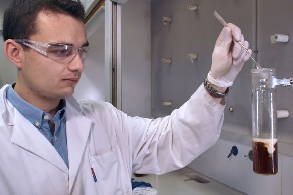 Forscher fügt Chemikalie in Glas mit dunkler Flüssigkeit hinzu