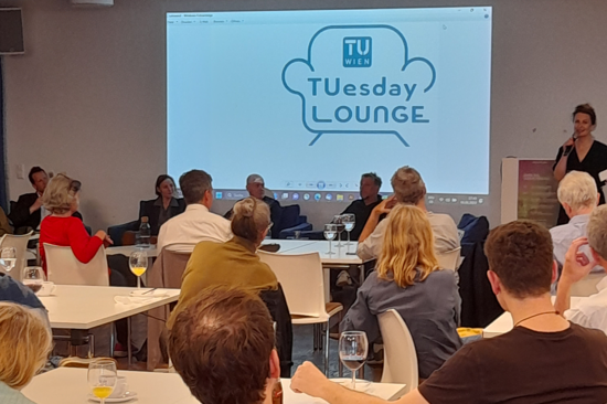 People sitting at tables and looking at a TUesday Lounge presentation.