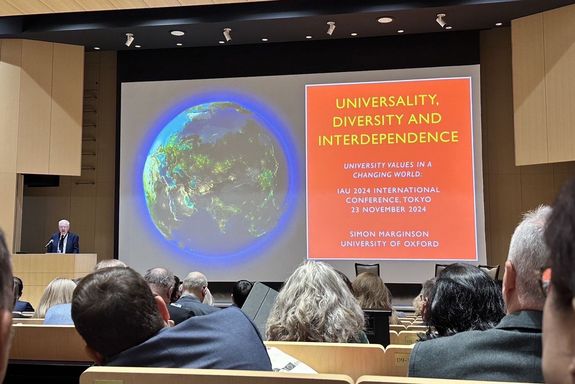 The photo was taken from the auditorium and shows a large hall with a speaker, the presentation and part of the audience.