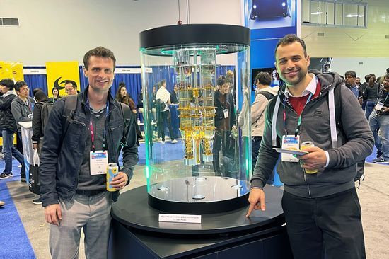 Two men are standing to the right and left of a large glass cylinder.