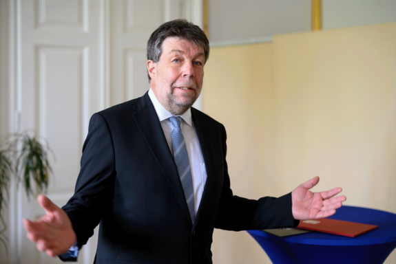 Peter Schöggl bei seiner Rede mit ausgebreiteten Händen. Er trägt einen dunklen Anzug, weißes Hemd und blaue Krawatte mit hellen Schrägstreifen.