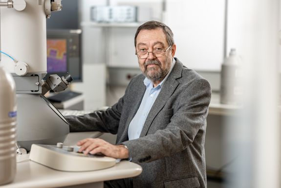 Forscher am Tisch sitzend, hinter einem Elektronenmikroskop