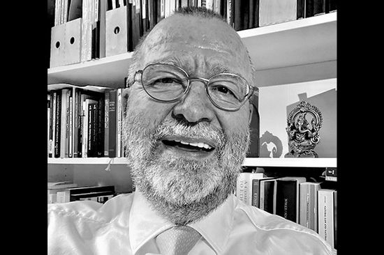 Schwarz-weiß Porträt eines älteren, lachenden Mannes mit gestutztem Vollbart. Dunkle Balken rechts und links