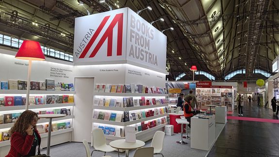Österreichischer Gemeinschaftstand auf der Frankfurter Buchmesse 2025: Man sieht den Stand der TU Wien Bibliothek. Man sieht einen großes Würfel mit "Books from Austria" aufgehängt. Darunter sind viele Regale mit Bücher, Standpulte und Sessel für Gespräche. 