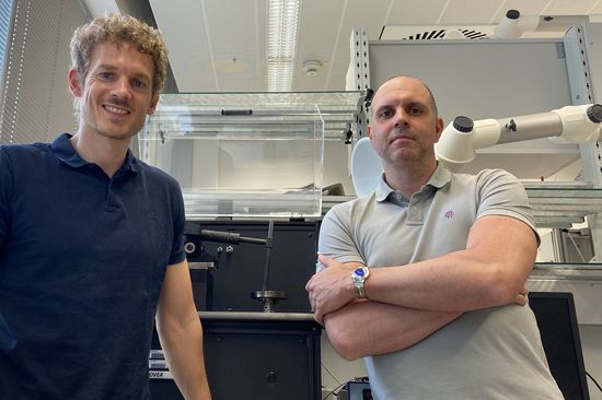 zwei Personen im Labor, dahinter ein Gerät